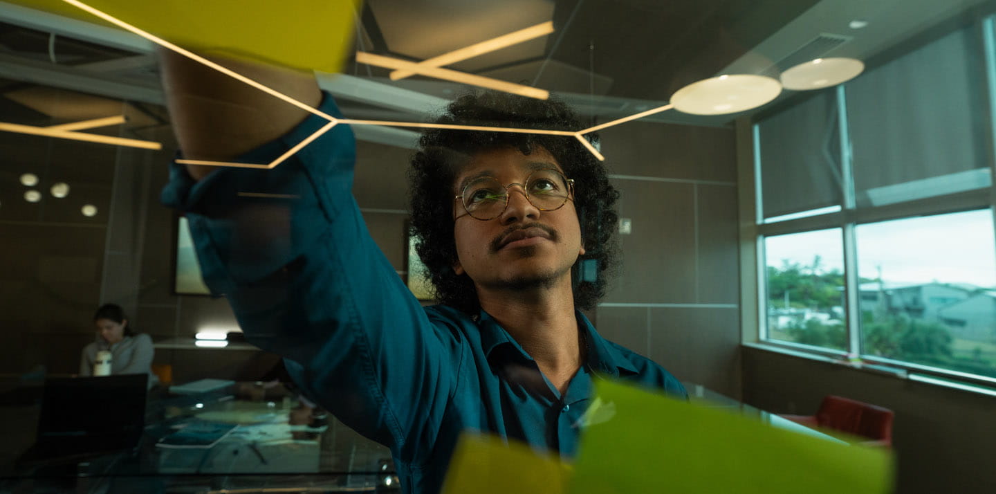 A person attaching sticky notes to a glass wall in a modern office.