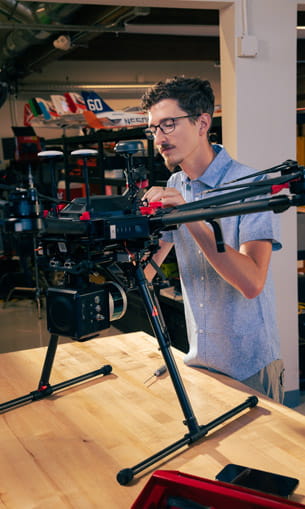 A person wearing protective glasses, working on a black drone.