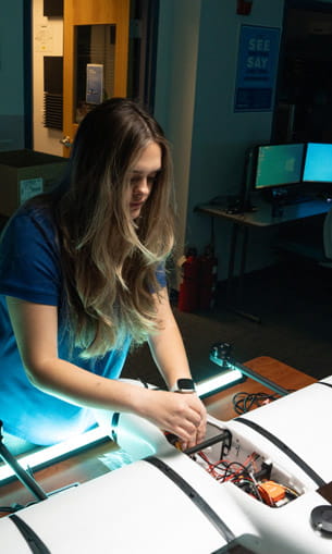 A person in a lab, working on a white drone.