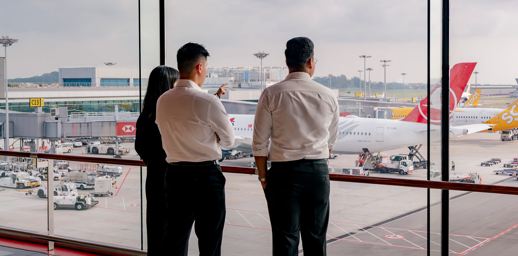 Three people look out a window at the airport tarmac