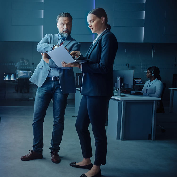 A man and woman looking at a laptop while a man sits at a desk behind them