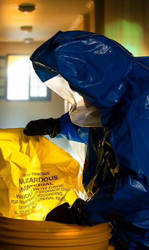 A person in a biohazard suit holding a Hazardous Materials bag