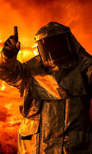 A person in a biohazard suit standing in front of a fire