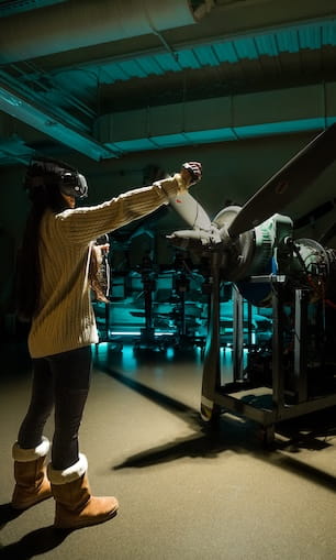 A student wearing a virtual reality headset and interacting with equipment in a laboratory environment.