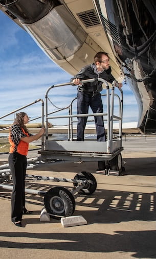 Students performing aircraft maintenance using mobile platform to access engine and underside of fuselage.