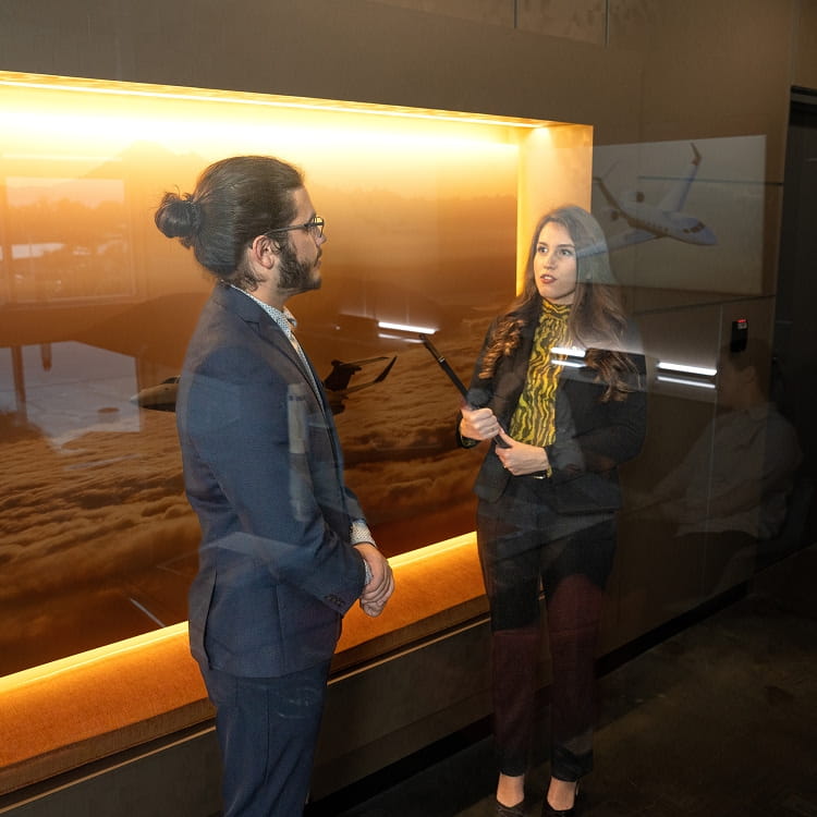 A woman speaking to a man in business attire while they stand in front of a large illuminated glass case.