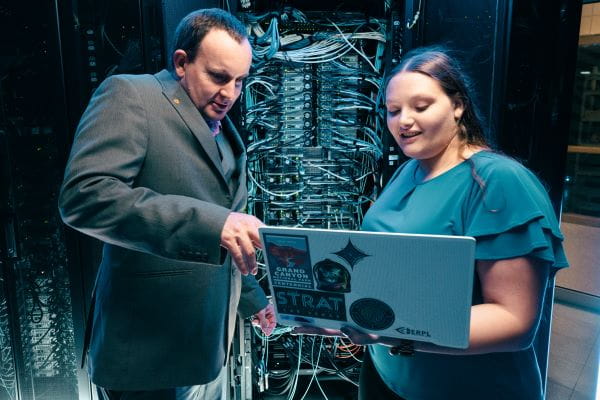 Two people in a server room working on a laptop.