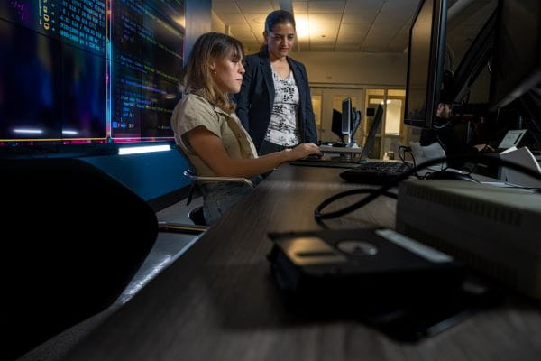Two people are working together on a laptop in a classroom.