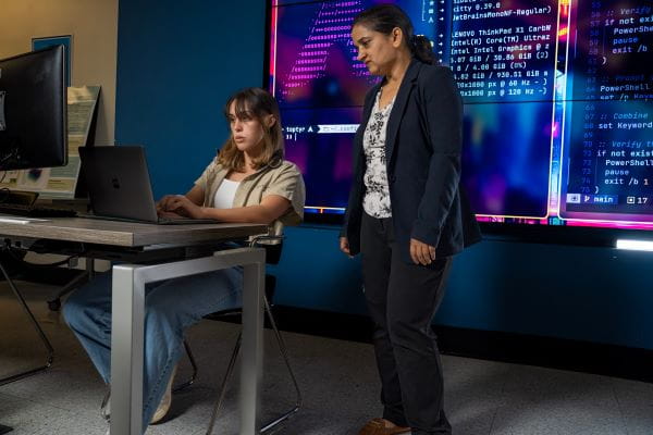 Two people are working together on a laptop in a classroom.