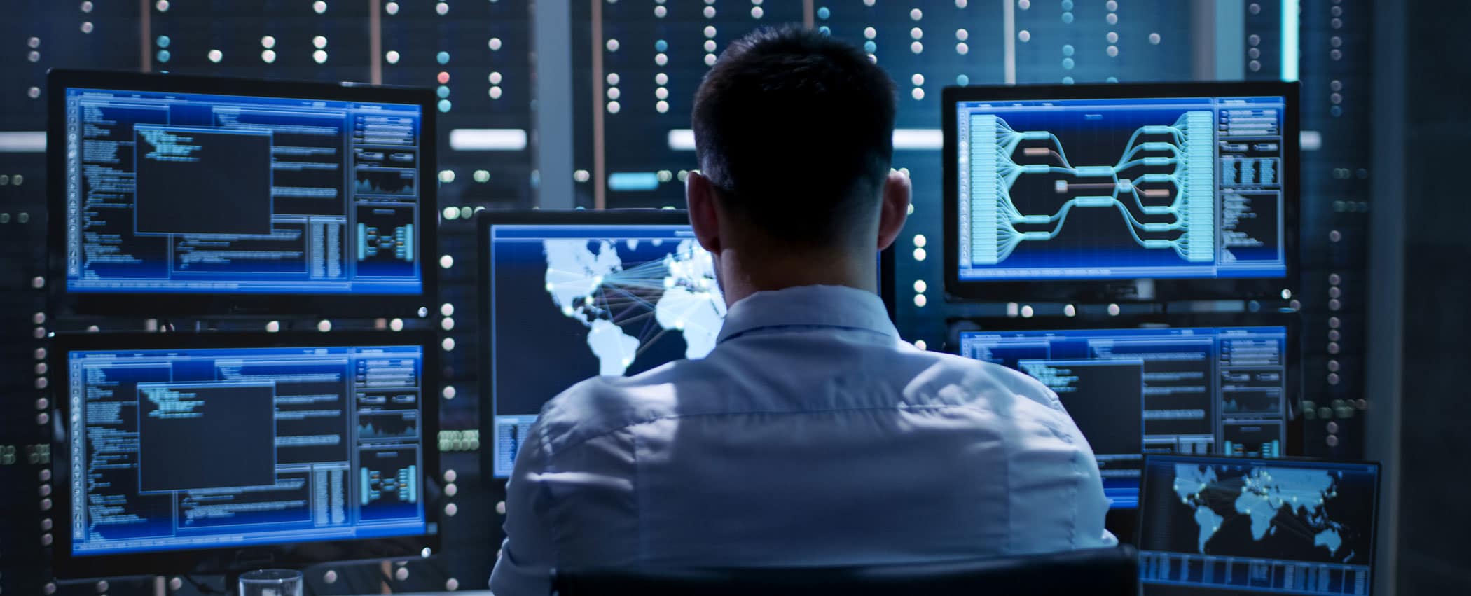 A person sits at a desk with five computer monitors displaying data on the screens.