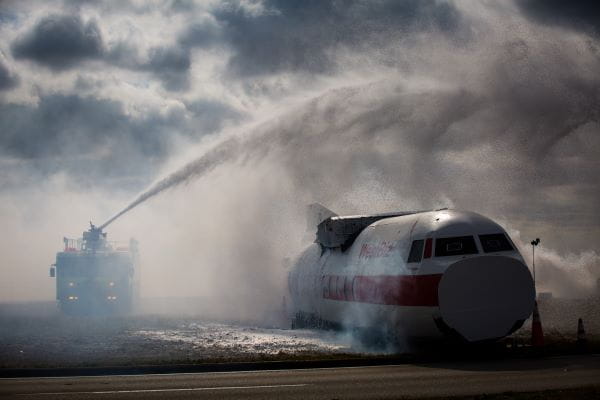Firefighters on a fire engine are spraying water onto an airplane.