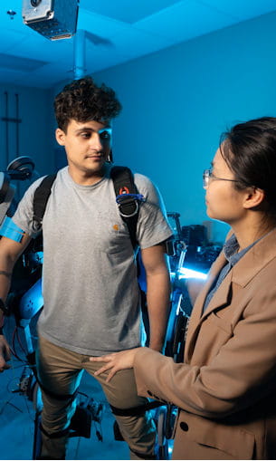 A mentor confers with a young man who is testing a device wrapped onto his body.