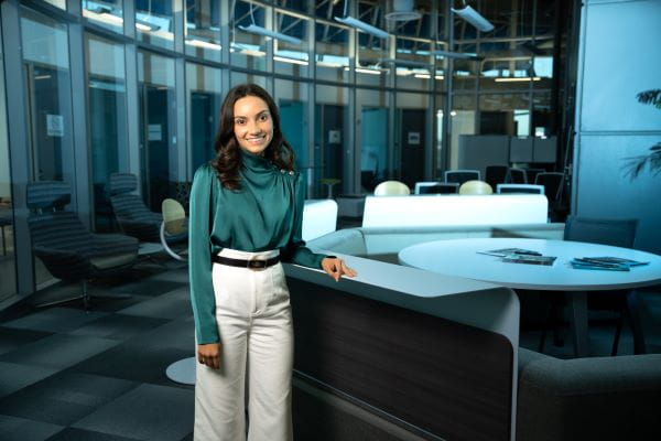 A person stands inside a building, leaning on a desk.
