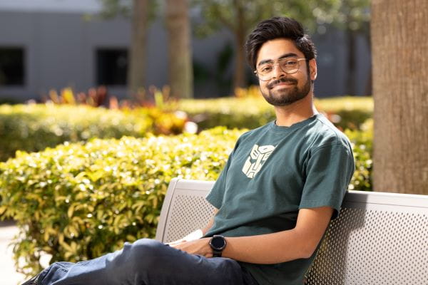 A person sits on an outdoor bench, smiling at the camera.