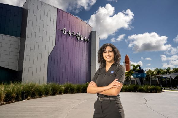 A person stands outside a building with their arms crossed.