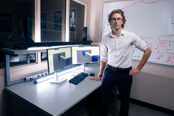 A person in business attire standing beside a desk with computer equipment.