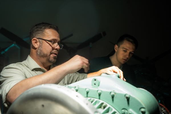 Two people working together to inspect and repair equipment in a dimly lit workspace.