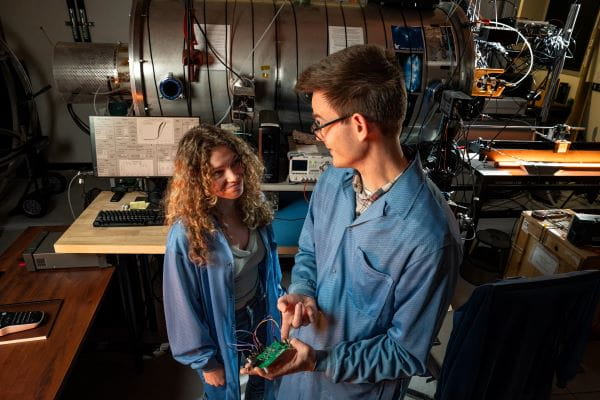 Two people in a workshop discussing a project, with tools and machinery in the background.