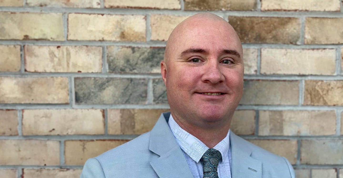 Charlie Woods wearing a business suit standing against a brick wall.