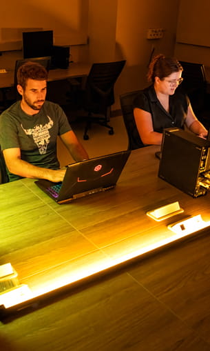 Two people sitting at a desk, working on laptops.