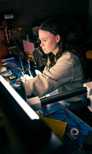 A person focuses on assembling or repairing electronic components at a workbench.