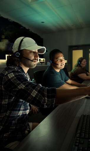 Three individuals operating equipment in a command and control center.