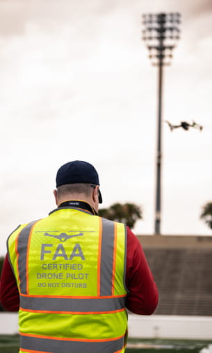 A person in a safety vest operating a drone outside.