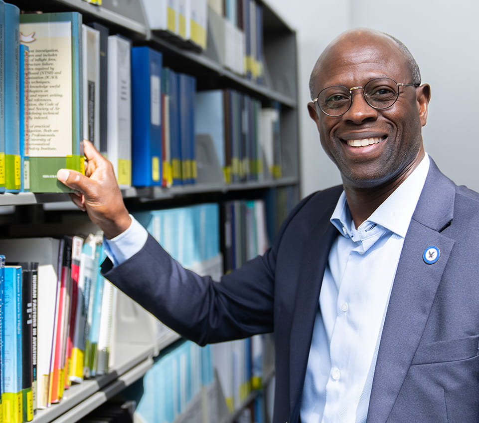 Staff member smiles at the camera, pulling a book from library shelves.
