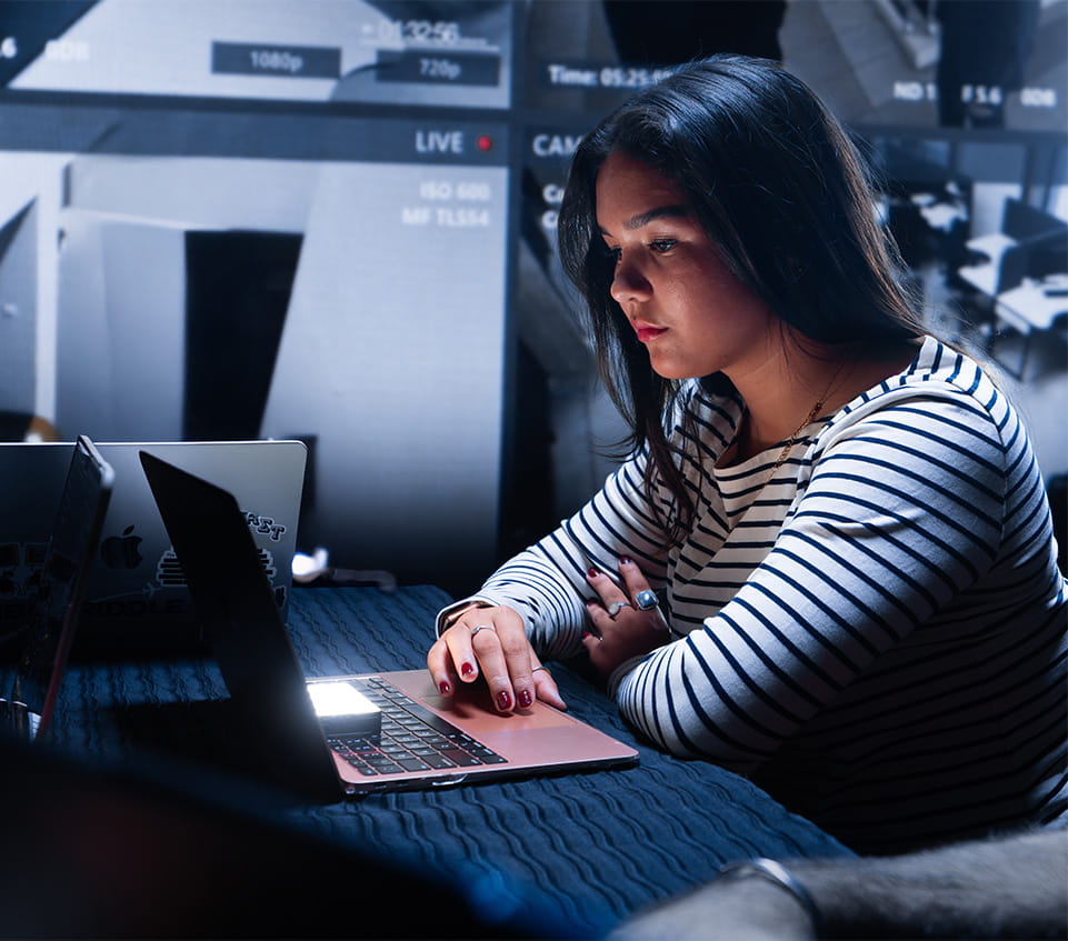 Student works at a laptop in front of a bank of video monitors.