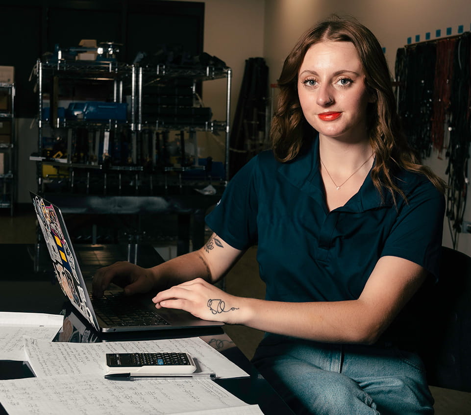 Student sits in a dark lab, working on her laptop covered in stickers.