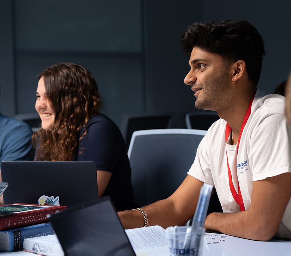 Two students study together, smiling at a third person off camera.