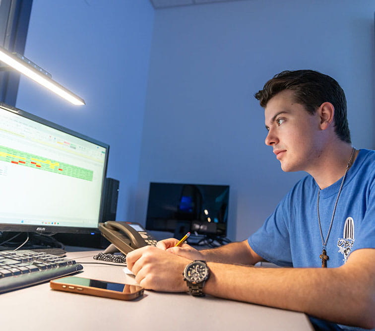 A student takes notes while looking at a chart on a computer screen