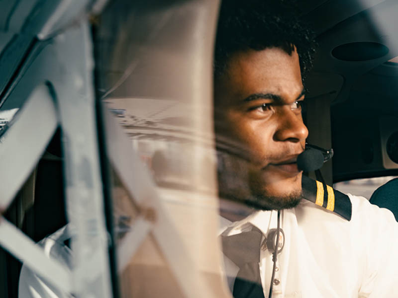 A pilot wears a headset and looks out of the cockpit window