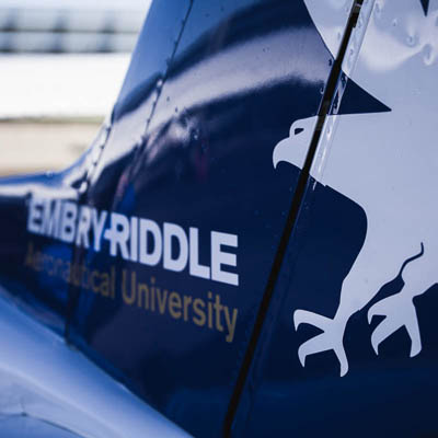 A close-up of the tail of a small aircraft displaying the text “Embry-Riddle Aeronautical University” and a white eagle emblem.