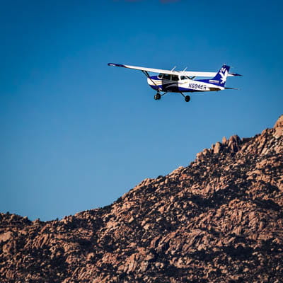 A small aircraft flying above a mountain beneath a blue sky.
