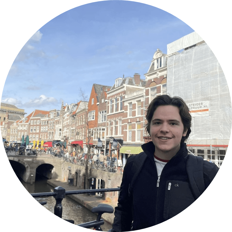Keelan Garde poses by a canal in the Netherlands with a stone bridge and rows of historic buildings in the background.