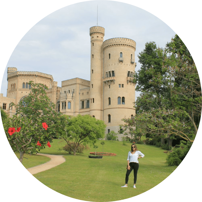 Mariana Palik Larranaga poses in Germany on a grassy lawn in front of a castle with towers and surrounding trees