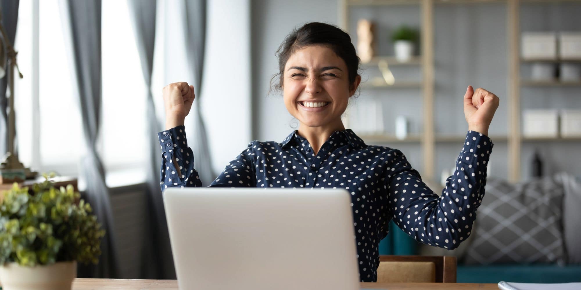 A graduate student celebrates their success in front of a laptop computer at home.