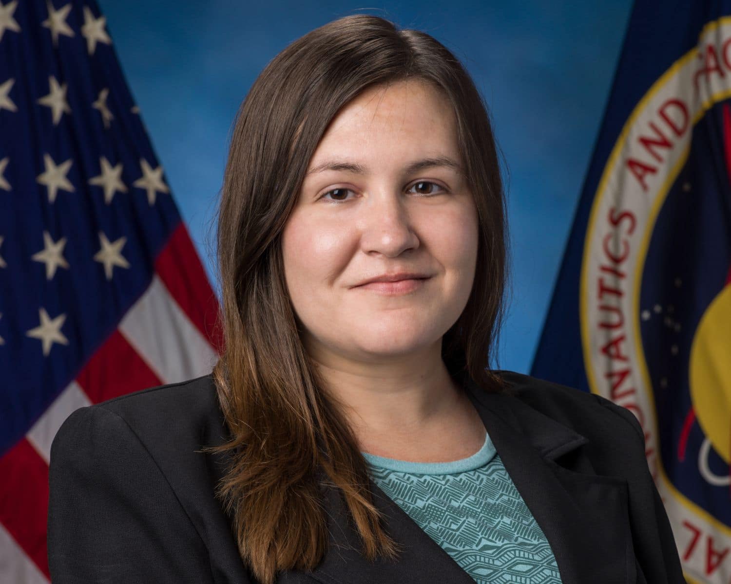 M.S. in Human Factors graduate Nicole Schoenstein in her official NASA photo with the American and NASA flags behind her. (Photo: Nicole Schoenstein)
