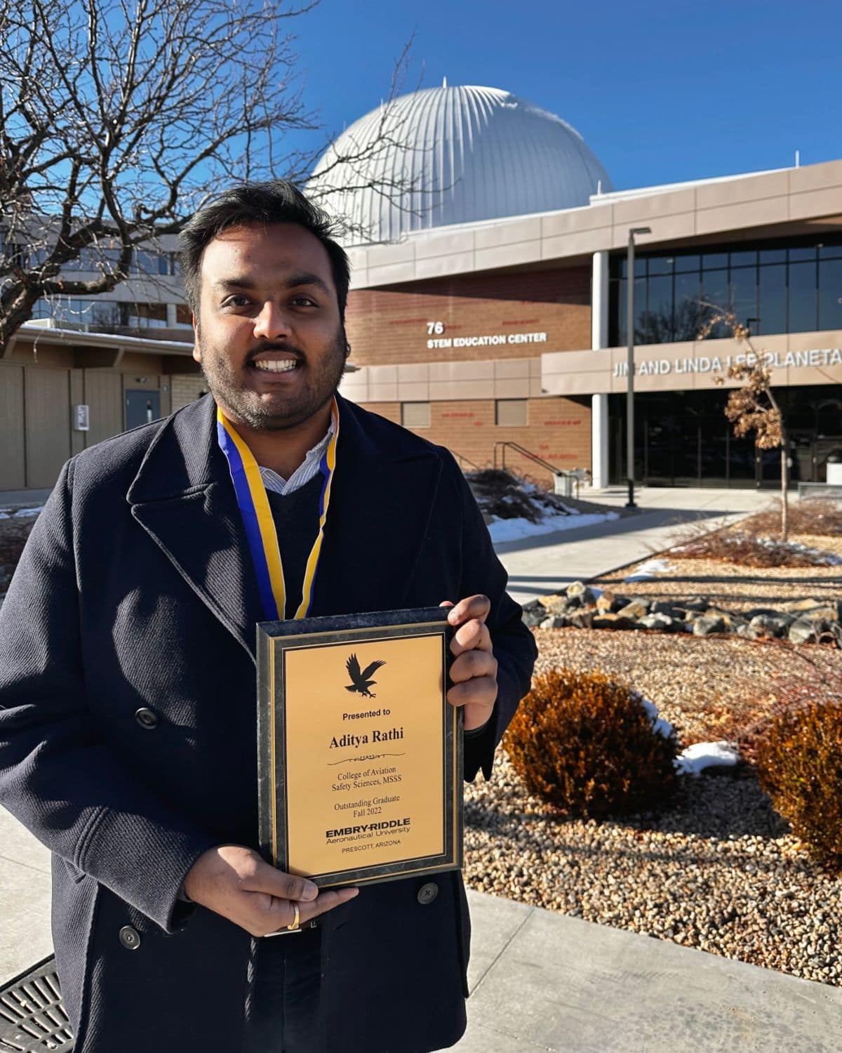 Aditya Rathi with his Distinguished Graduate award, in front of Embry‑Riddle Prescott’s Jim and Linda Lee Planetarium. (Photo: Aditya Rathi)