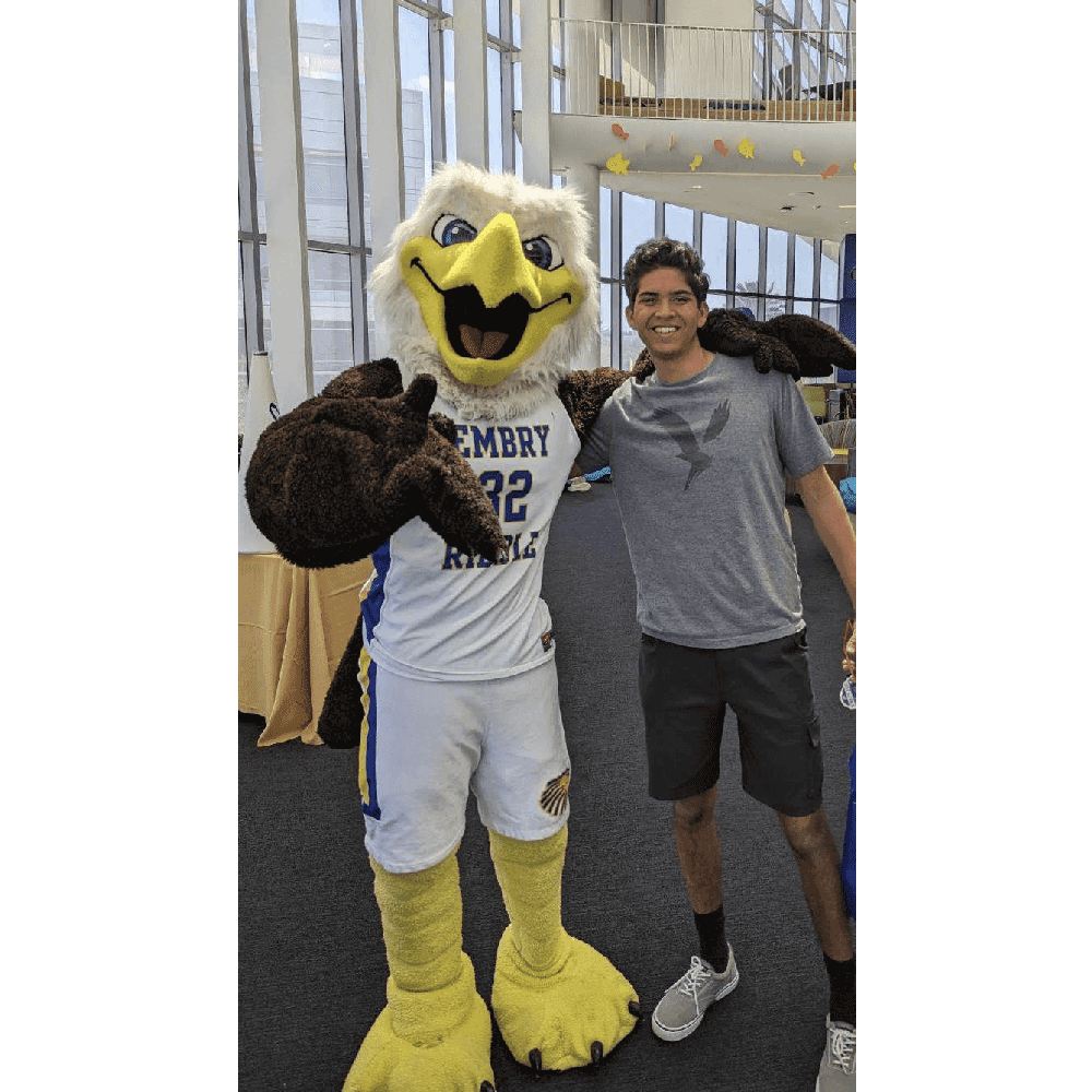 Adam, in shorts and a eagle t-shirt, stands next to the eagle mascot, who wears a basketball uniform.