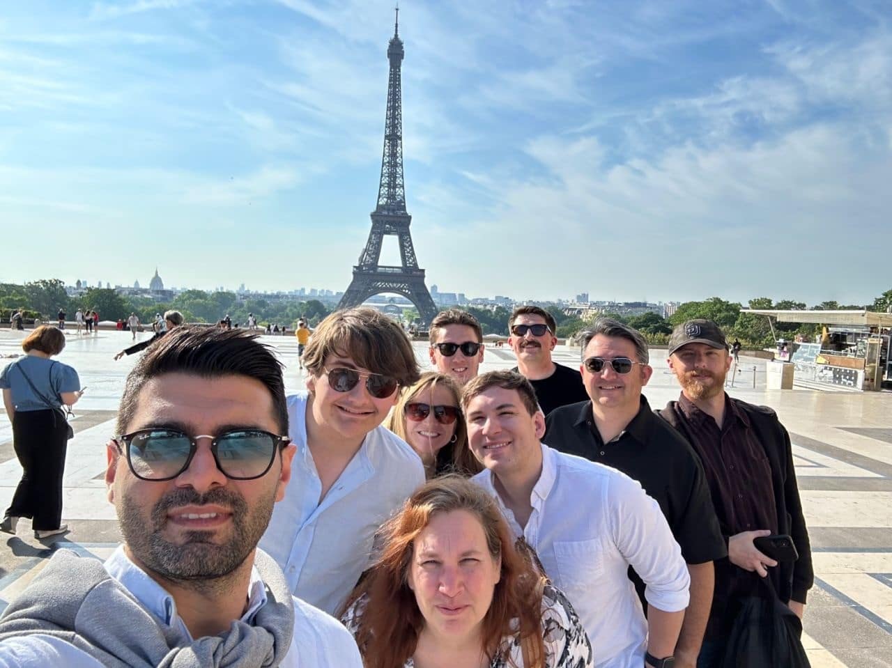 Several students squeeze together for a selfie, the Eiffel Tower in the background.