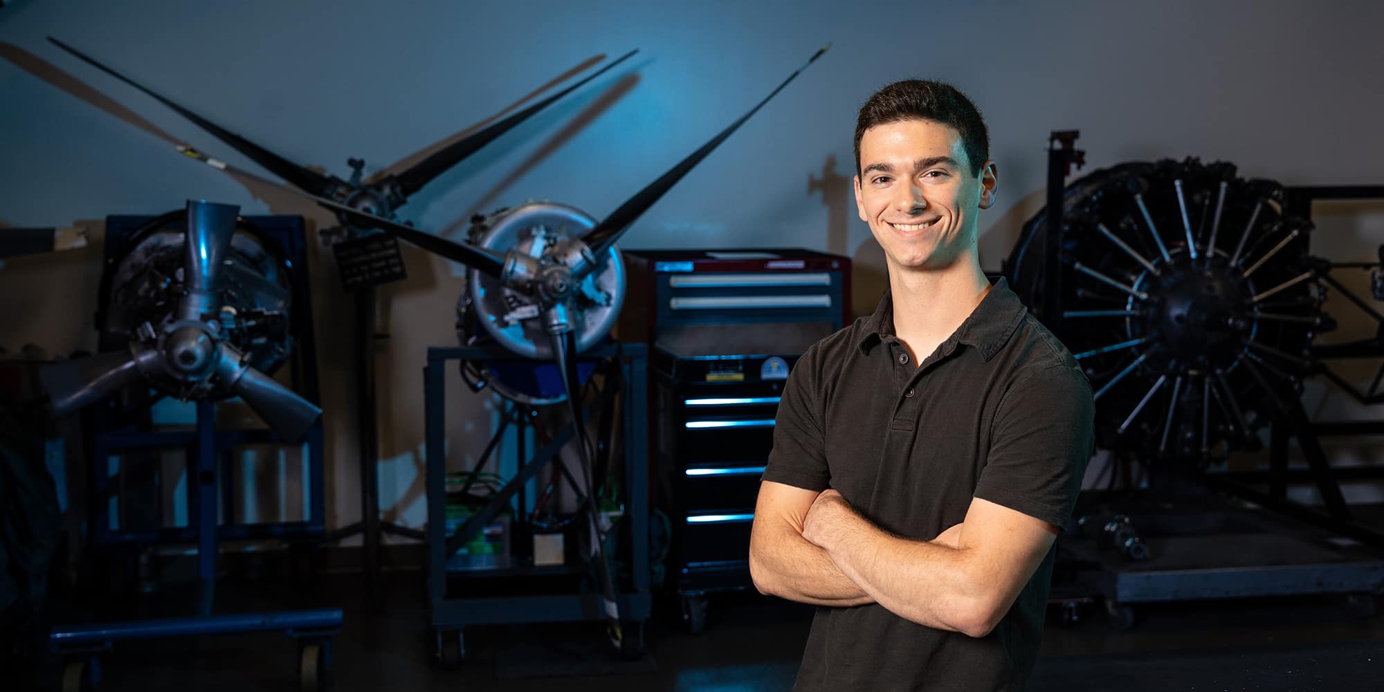 Nicolas Napoleoni poses in a dark polo shirt in front of several propellers and engines.