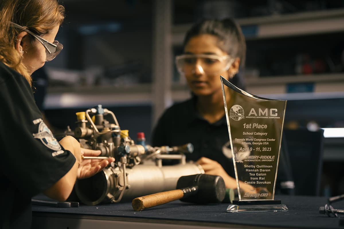 The Aerospace Maintenance Competition first-place trophy that Shelby and her teammates won is displayed in one of the AMS labs as Hannah Daren (left) and Iram Rai work in the background. (Embry-Riddle Photo/Bill Fredette-Huffman)