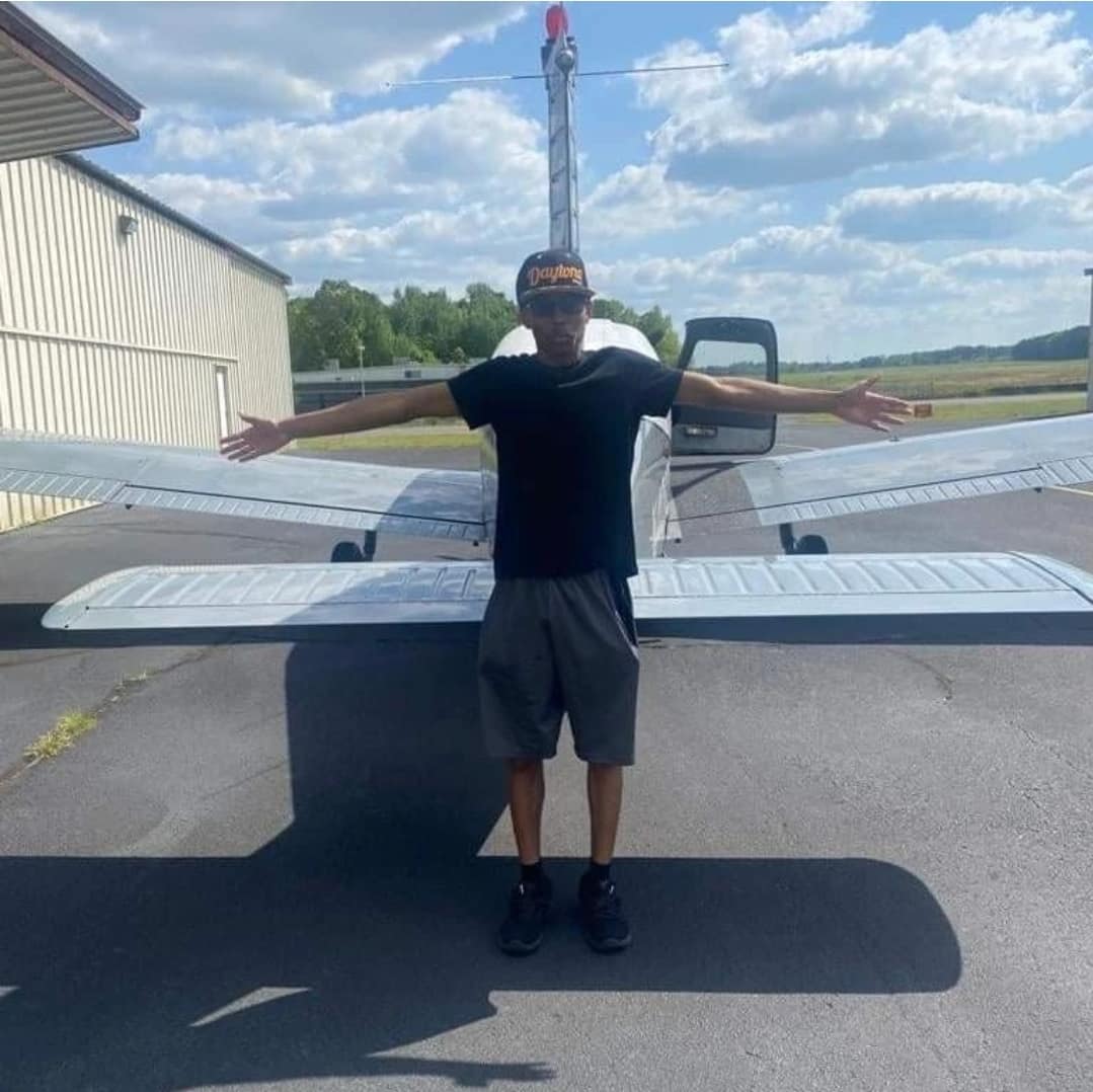 Sporting a “Daytona” baseball cap, Josiah Mosie strikes his best airplane pose while standing behind a single-engine aircraft. (Photo: Josiah Moise)
