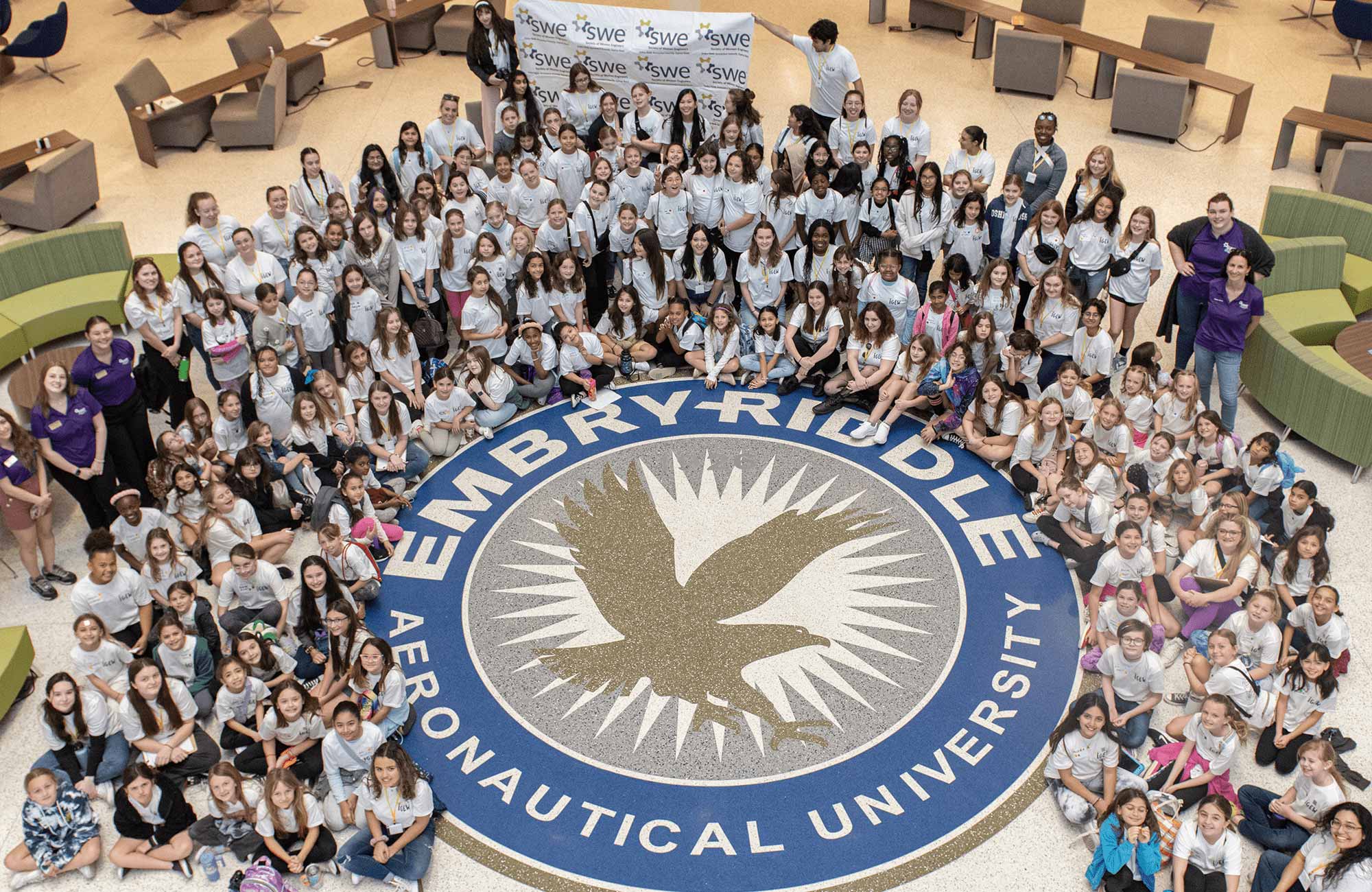 Young girls from Volusia County pose around the Embry‑Riddle seal in the Mori Hosseini Student Union during the Introduce a Girl to Engineering Workshop (IGEW) led by the Society of Women Engineers (SWE) Collegiate Section at the Daytona Beach campus on Feb. 17, 2024. (Photo: Embry‑Riddle)