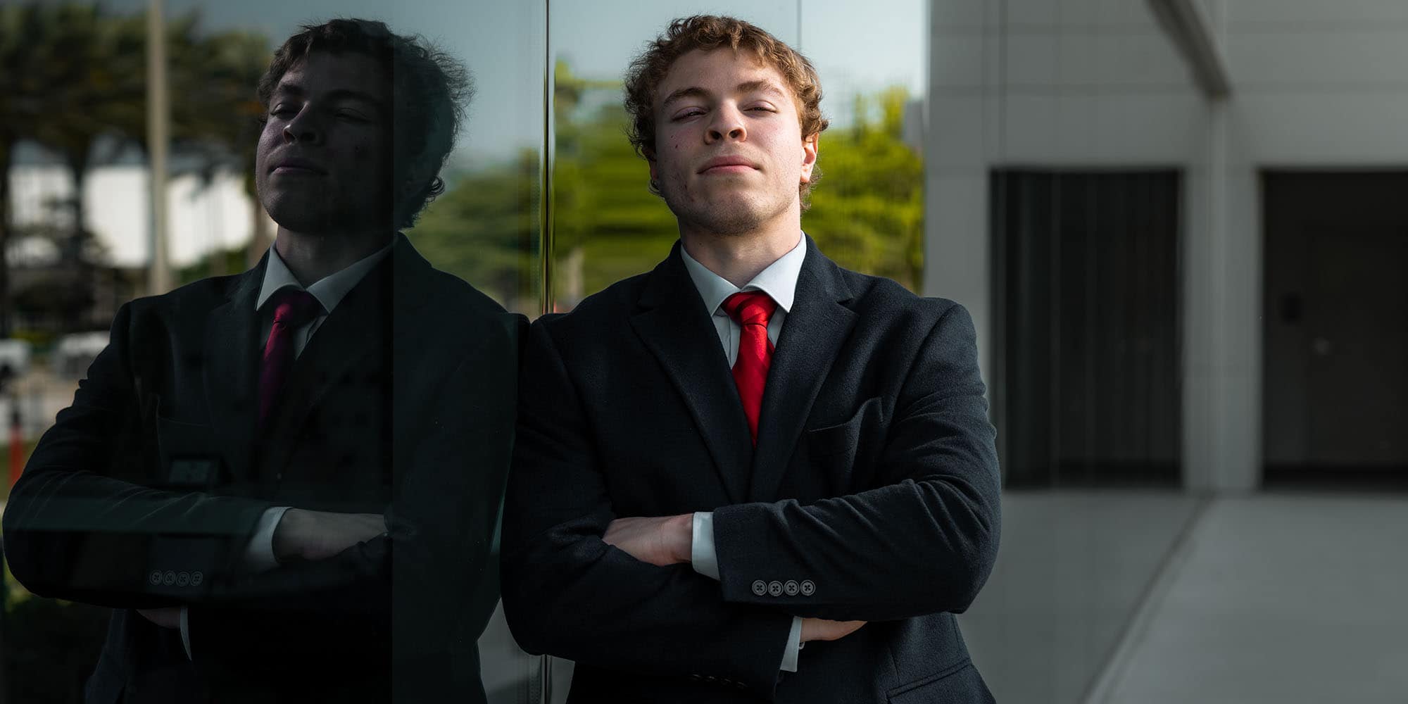Javier Morales poses against a wall of windows outdoors, in a dark business suit and red tie, looking defiantly at the camera.