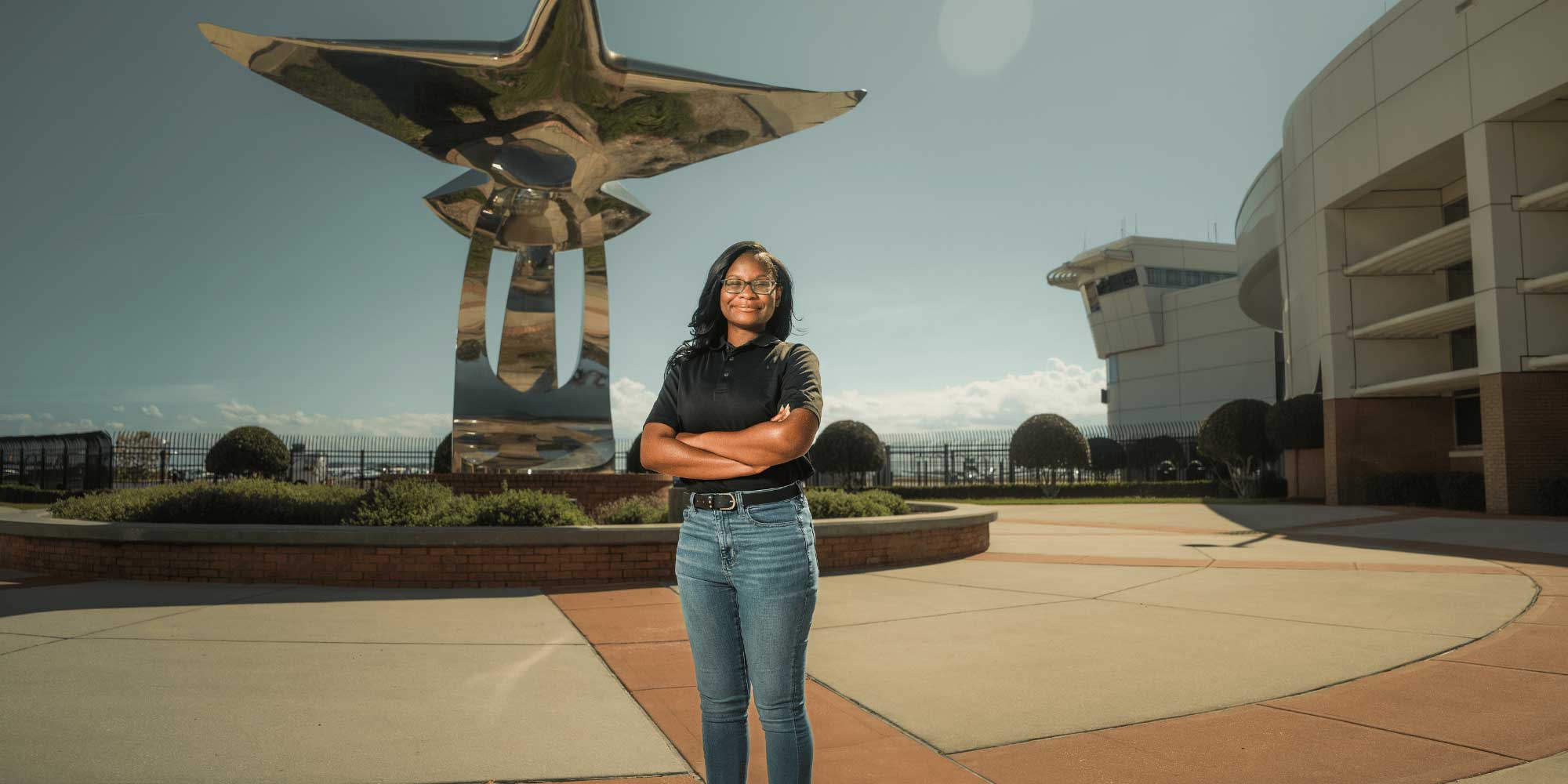 Olivia Munisi stands confidently in front of the silver plane/bird sculpture on the Daytona Beach Campus, Pathways to the Sky.