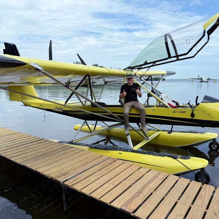 Man sits on yellow seaplane floating next to dock.