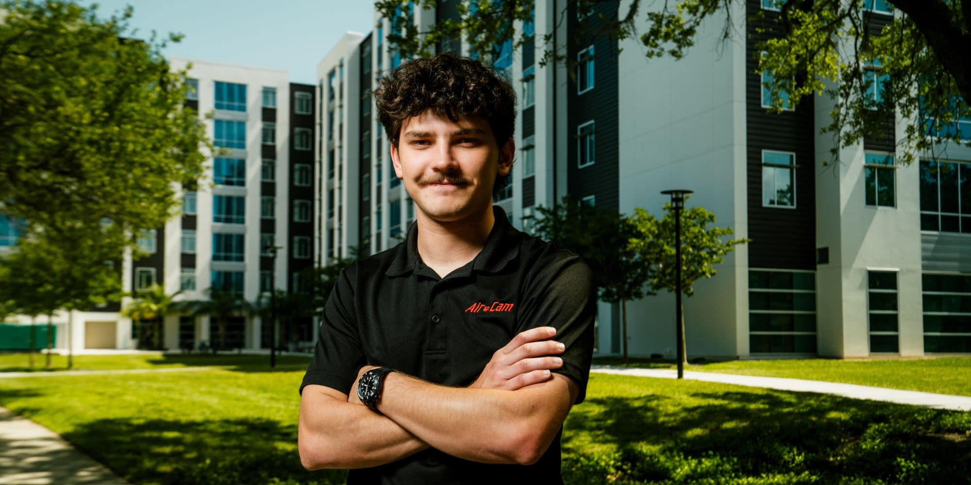 Man stands with arms crossed in front of student housing building.